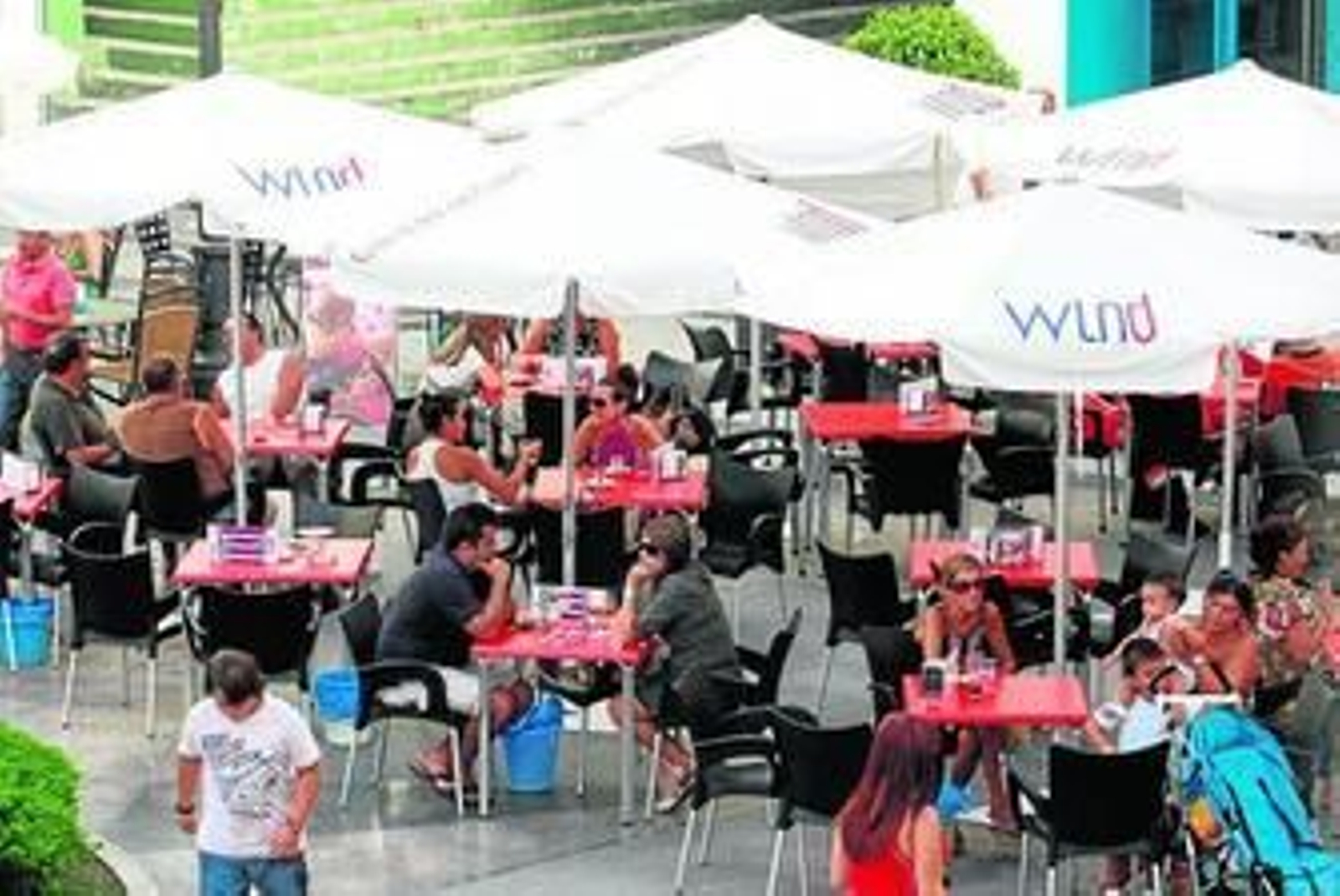 Mesas de una terraza en la plaza de la Iglesia, mientras los vecinos disfrutan del ambiente con la mejor compañía.