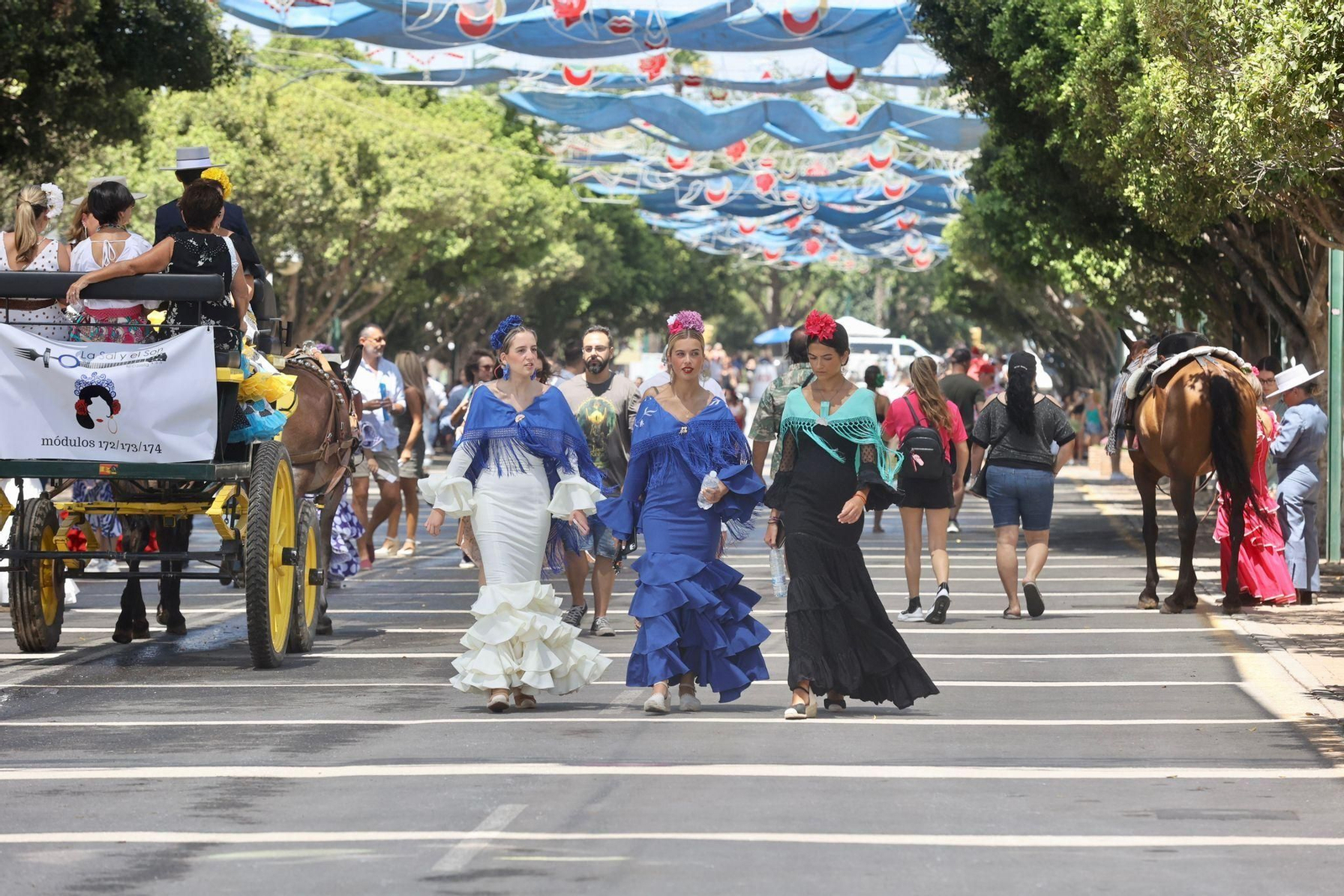 Tres chicas vestidas de flamenca pasean por el Real.