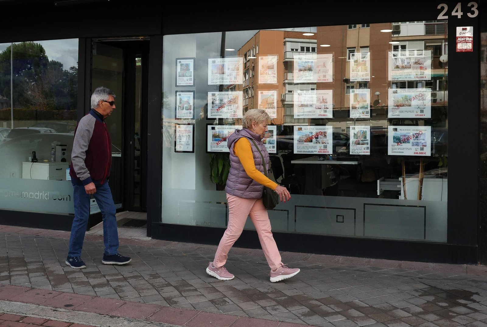 Dos personas caminan por delante de un escaparate de una inmobiliaria.