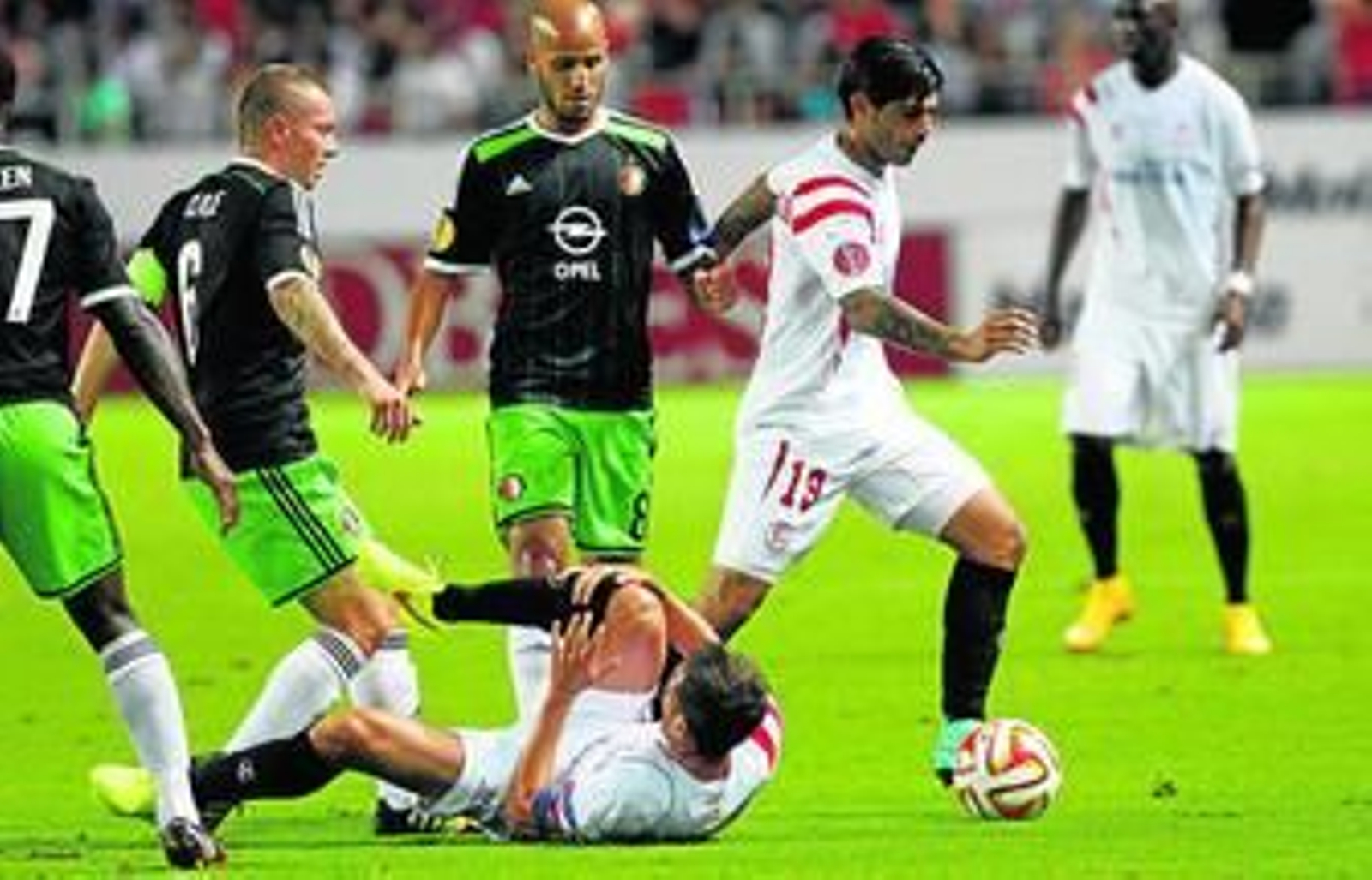 Banega avanza con el balón mientras Fernando Navarro se protege caído en el suelo.