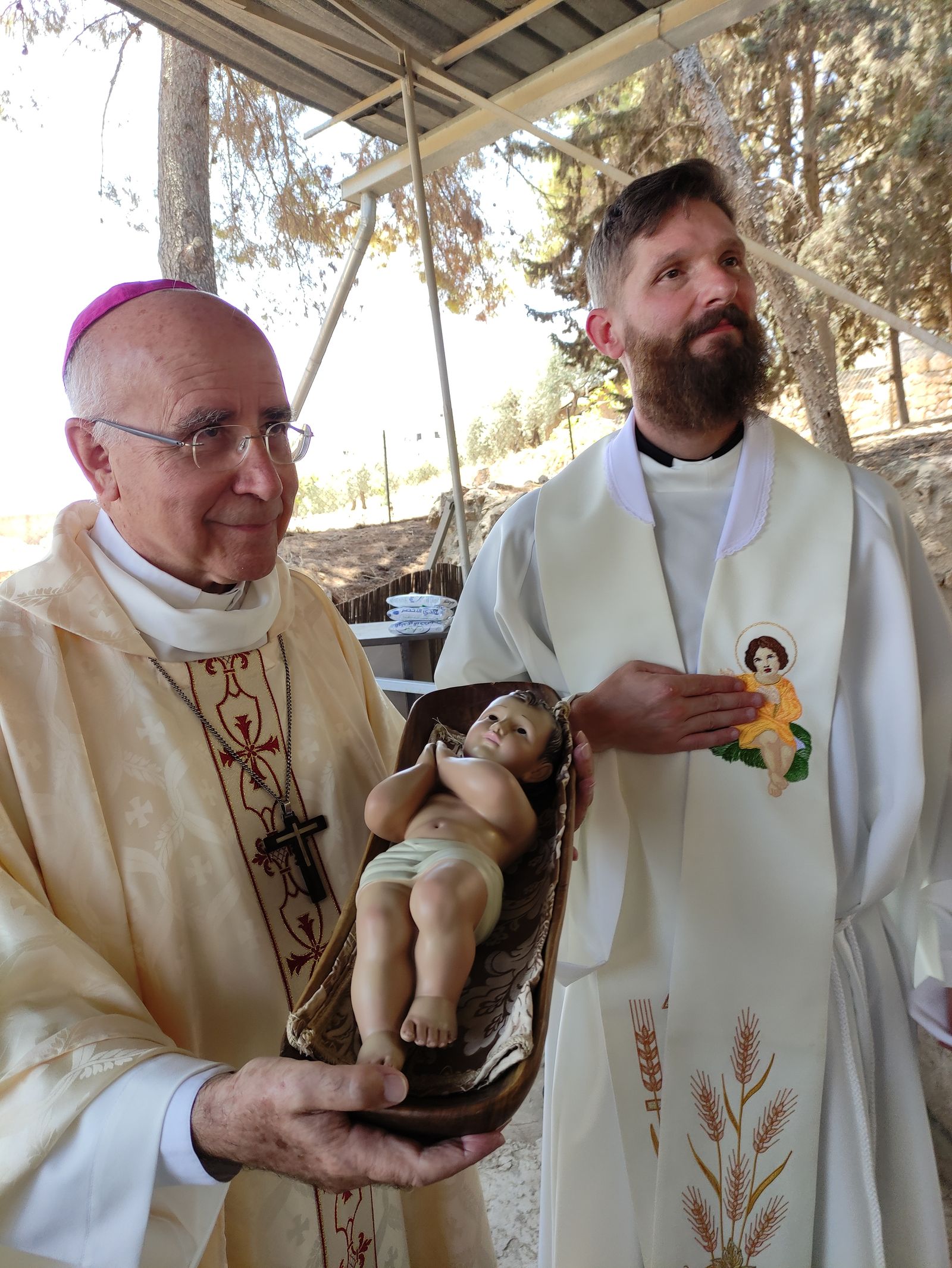 El obispo emérito José Vilaplana muestra a la adoración al Niño Jesús en el Campo de los Pastores, acompañado por el sacerdote Servando Pedrero.