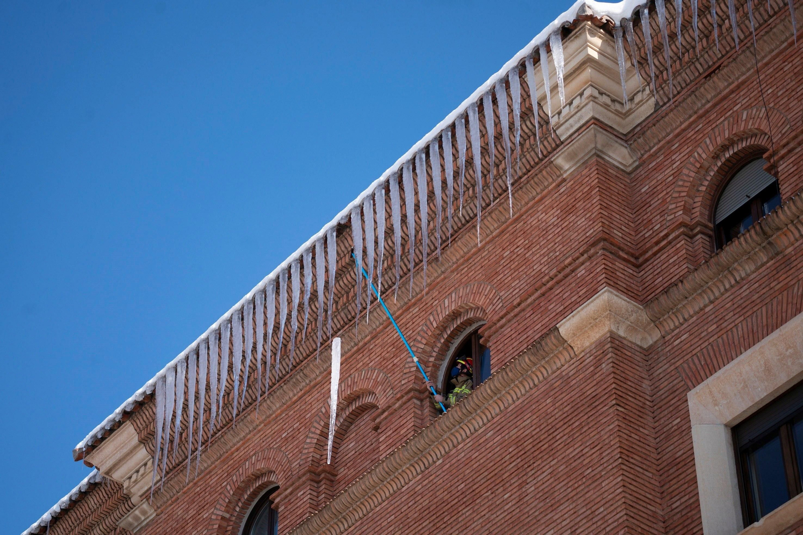 Un bombero retira carámbanos de hielo de la cornisa de un edificio en Teruel.