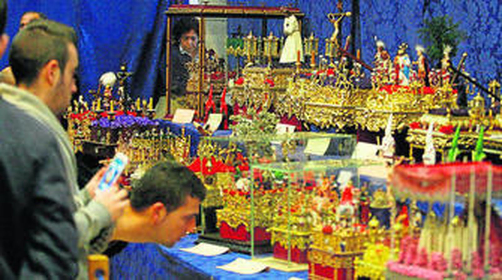 Varios visitantes observan con interés algunas de las 106 obras que componen esta muestra de modelismo cofrade.