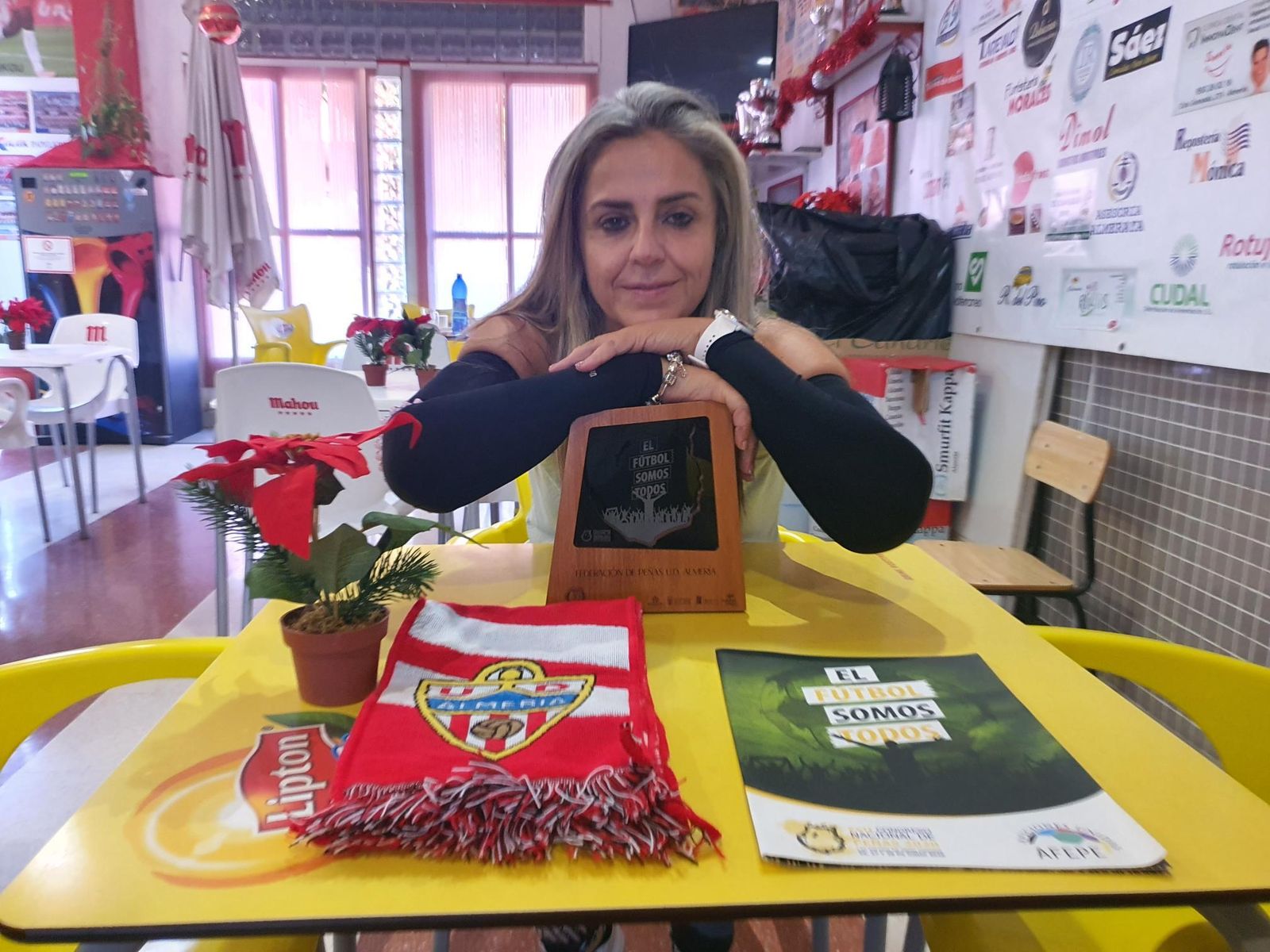 Mónica, en la sede de su peña, con una bufanda del Almería y una metopa y una carpeta de Aficiones Unidas.