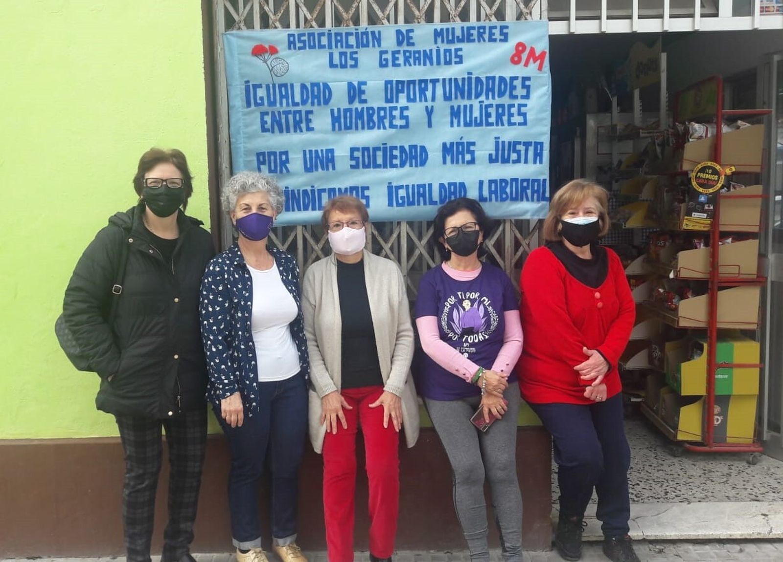 Mujeres de la asociación Los Geranios, junto a la pancarta instalada con motivo del 8-M.