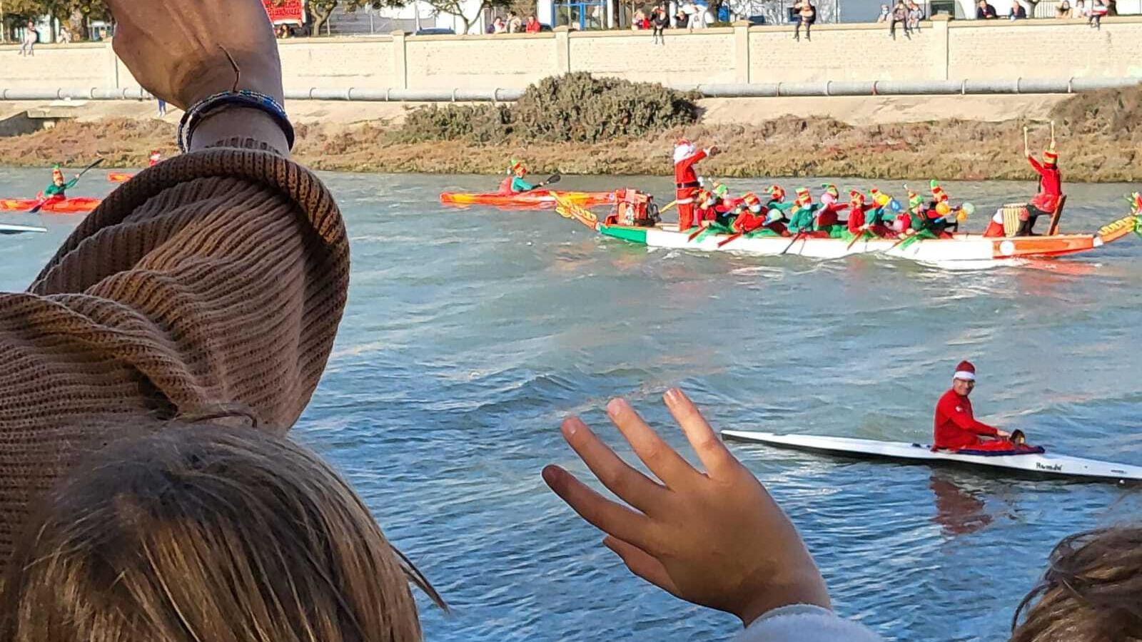 Varias personas saludan a las embarcaciones durante el desfile.