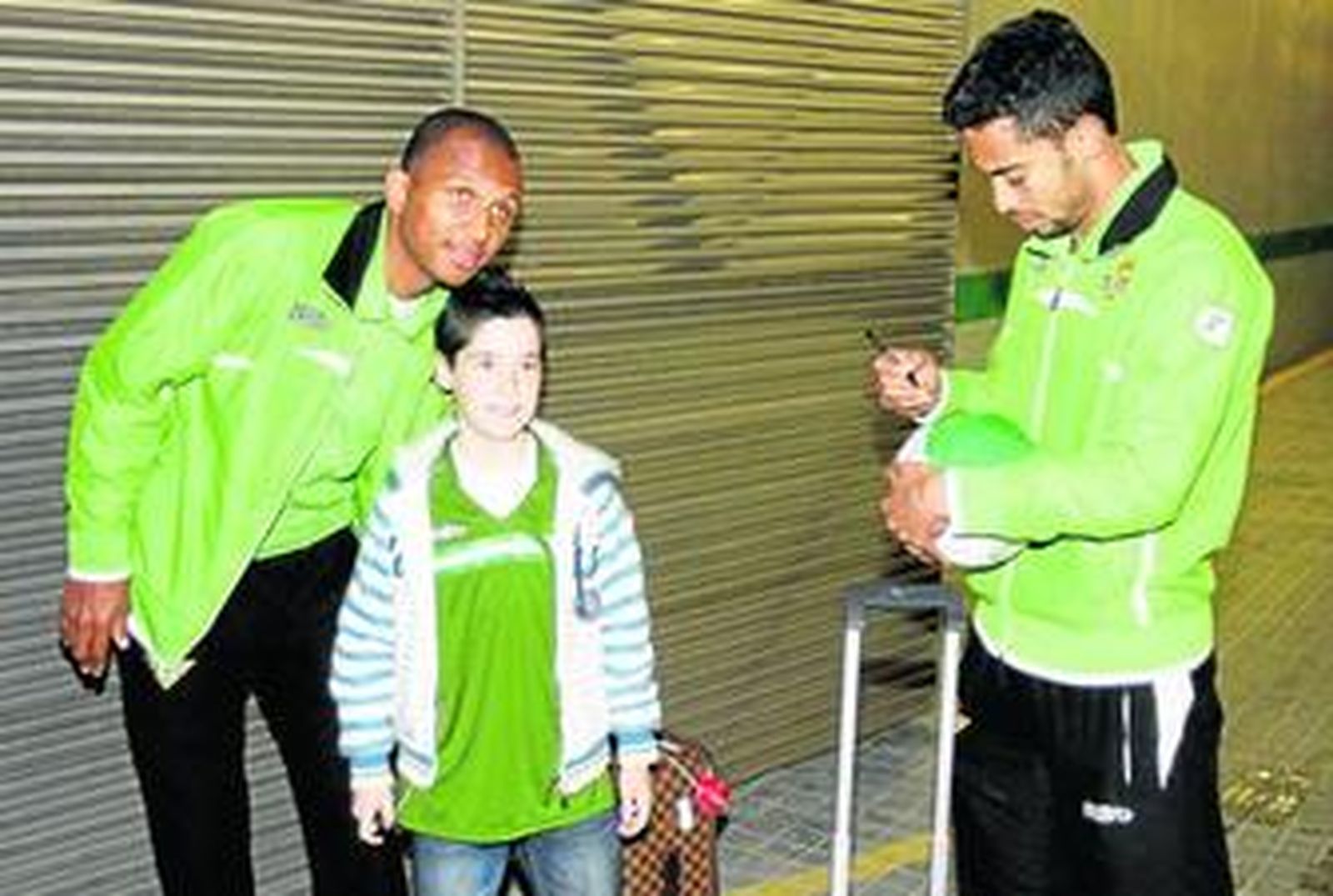 Un niño se fotogarfía con Mehmet Aurelio mientras Iriney, el hombre que ha perdido el sitio en favor del brasileño, le firma un balón.