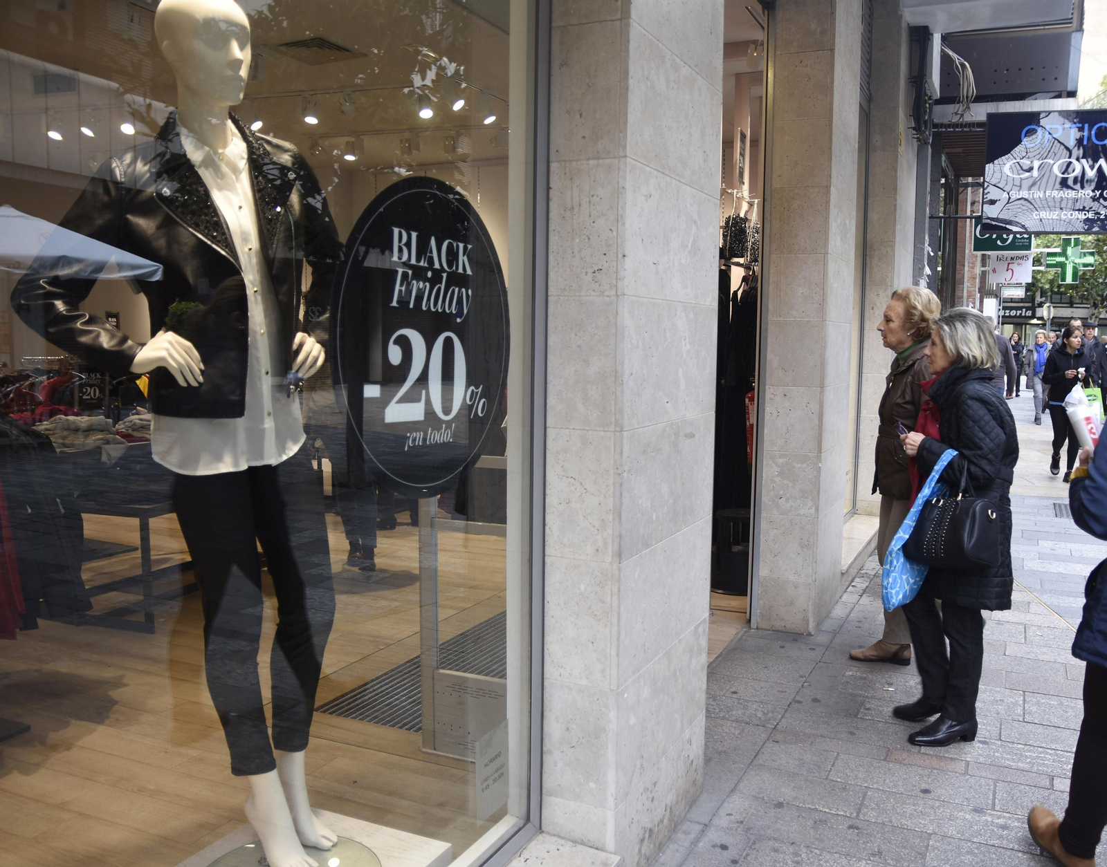 Dos señoras observan el escaparate de una tienda donde ya pueden verse los anuncios de descuentos por el Black Friday.
