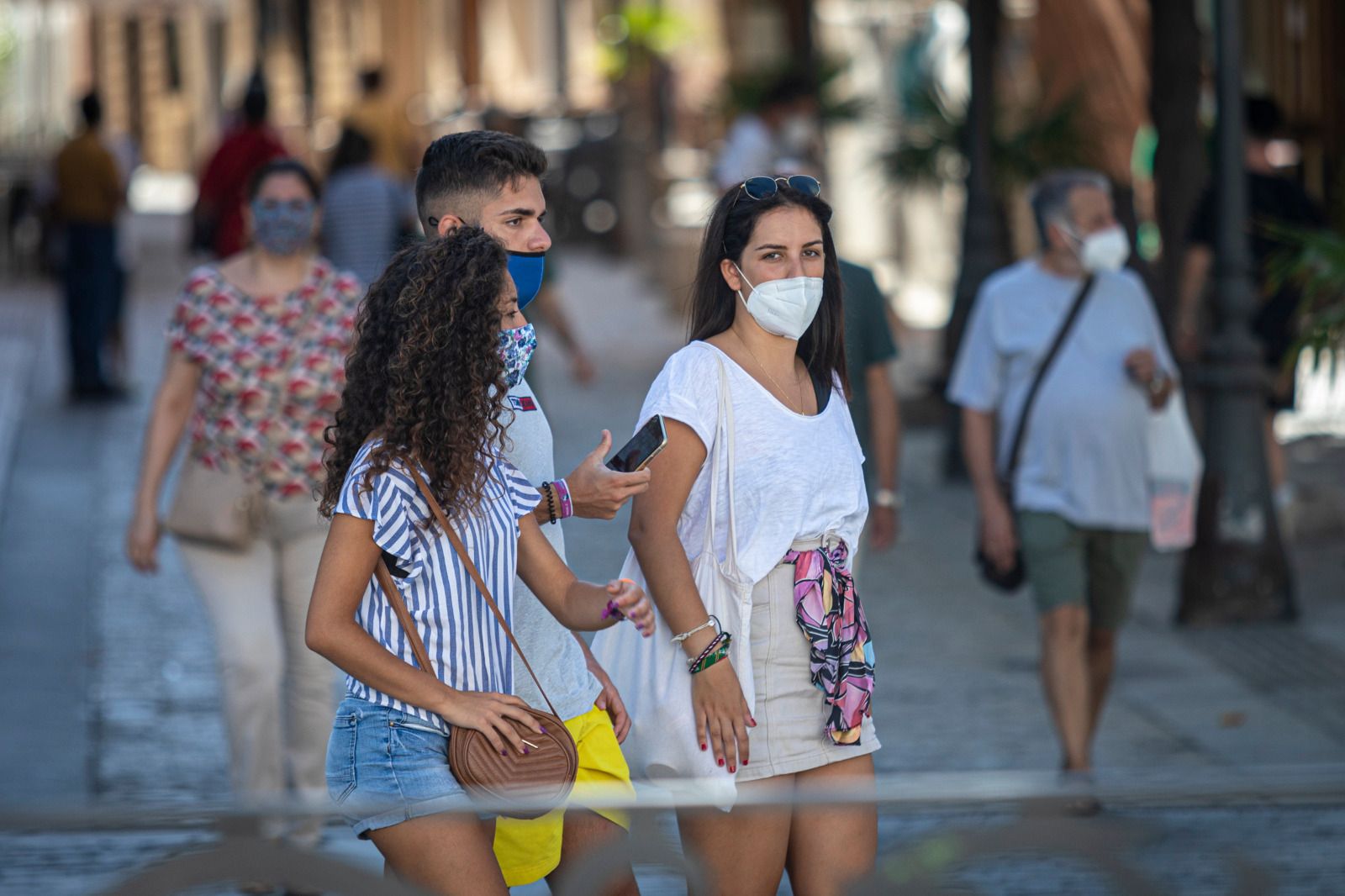 Jóvenes con mascarillas pasean por una calle de Cádiz.