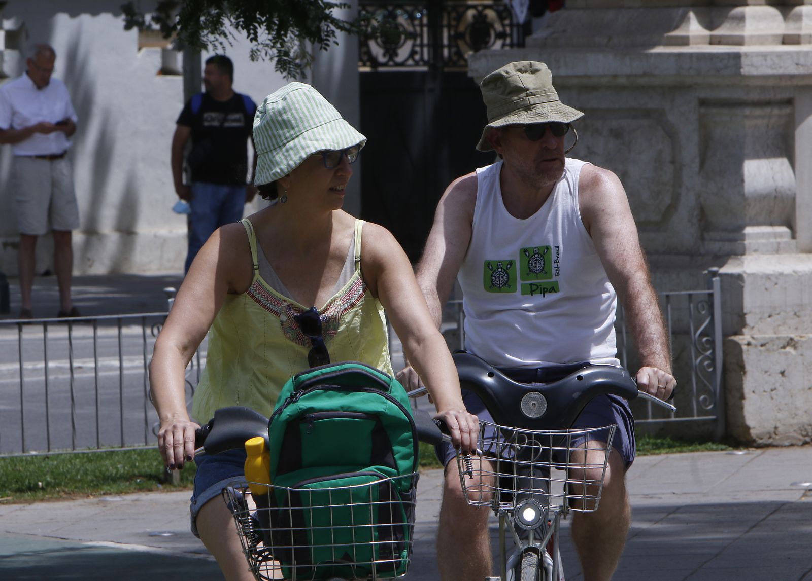 Dos turistas con gorro montados en bici al sol.