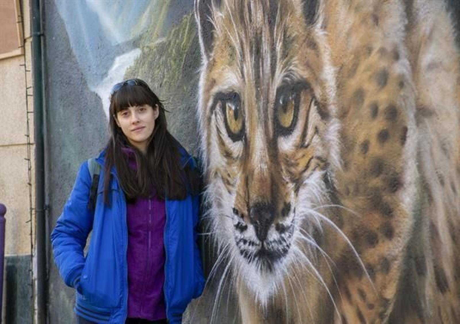 La artista Icat (Mónica Gómez Martínez) posa ante un mural suyo de un lince.