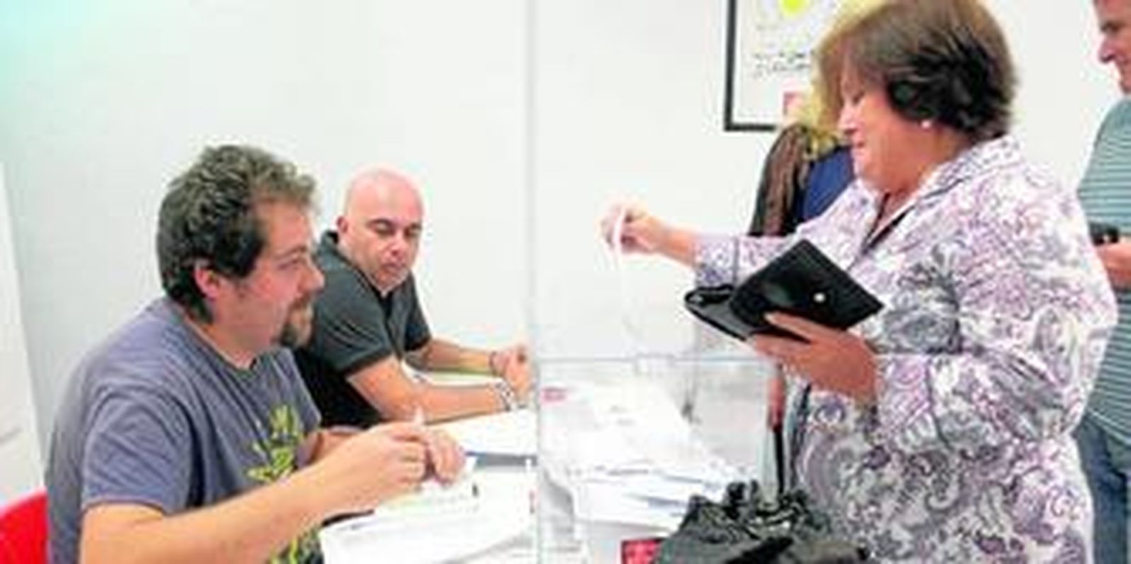 Una de las personas que participó ayer en las primarias se dispone a depositar su voto en la urna ante la mirada de uno de los candidatos, David Navarro, al fondo.