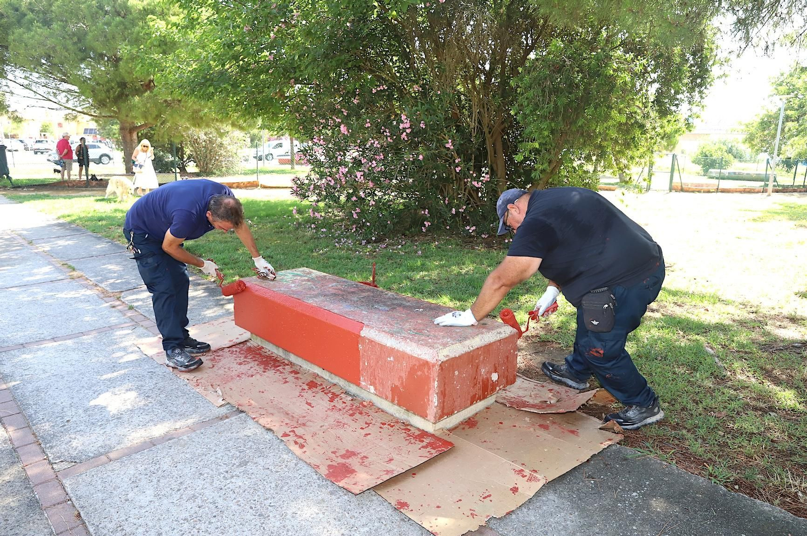 Dos operarios municipales, pintando uno de los bancos.
