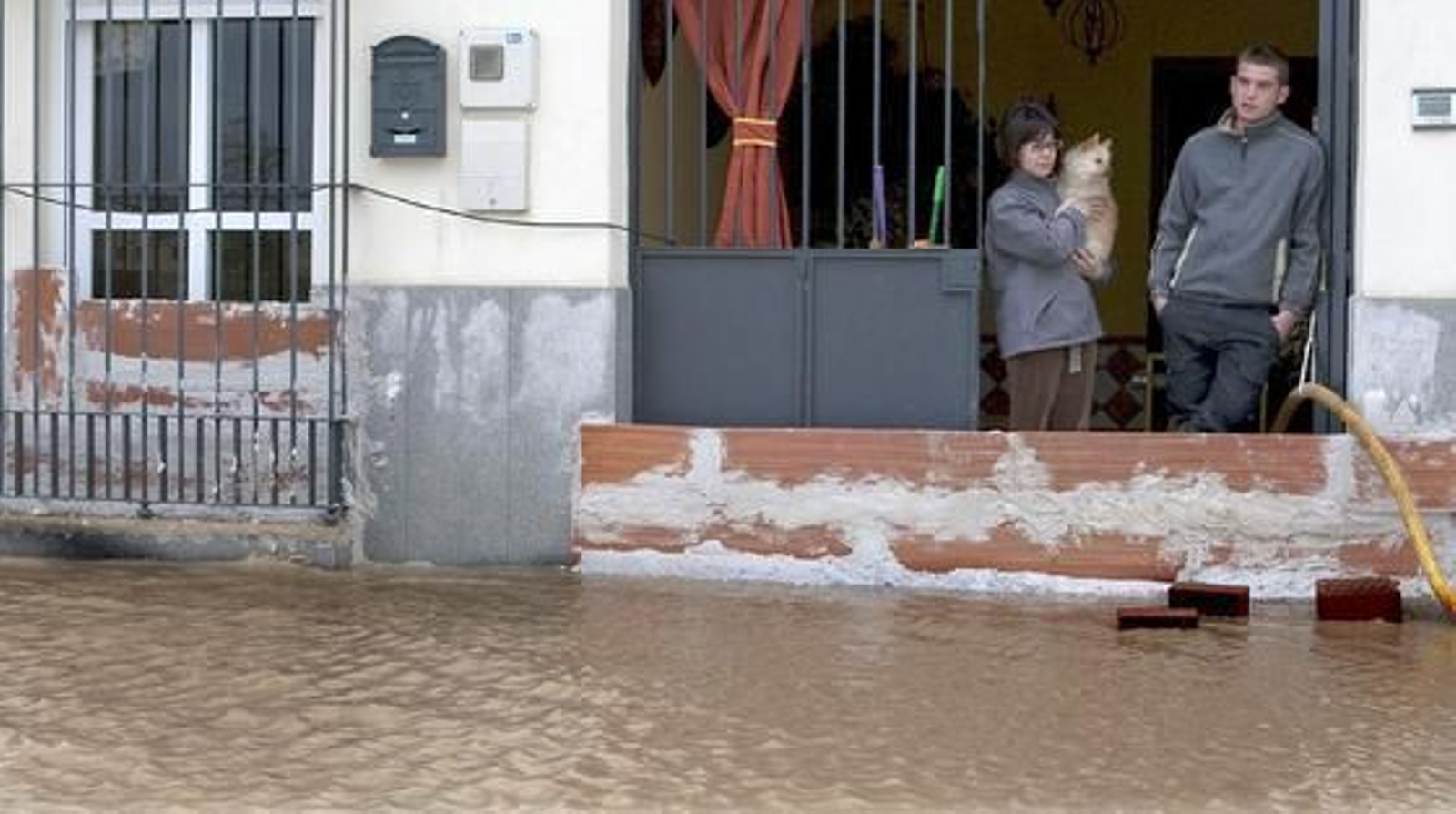 Una familia de Lora del Río asomada a la calle, cubierta totalmente por el agua.

Foto: Agencias