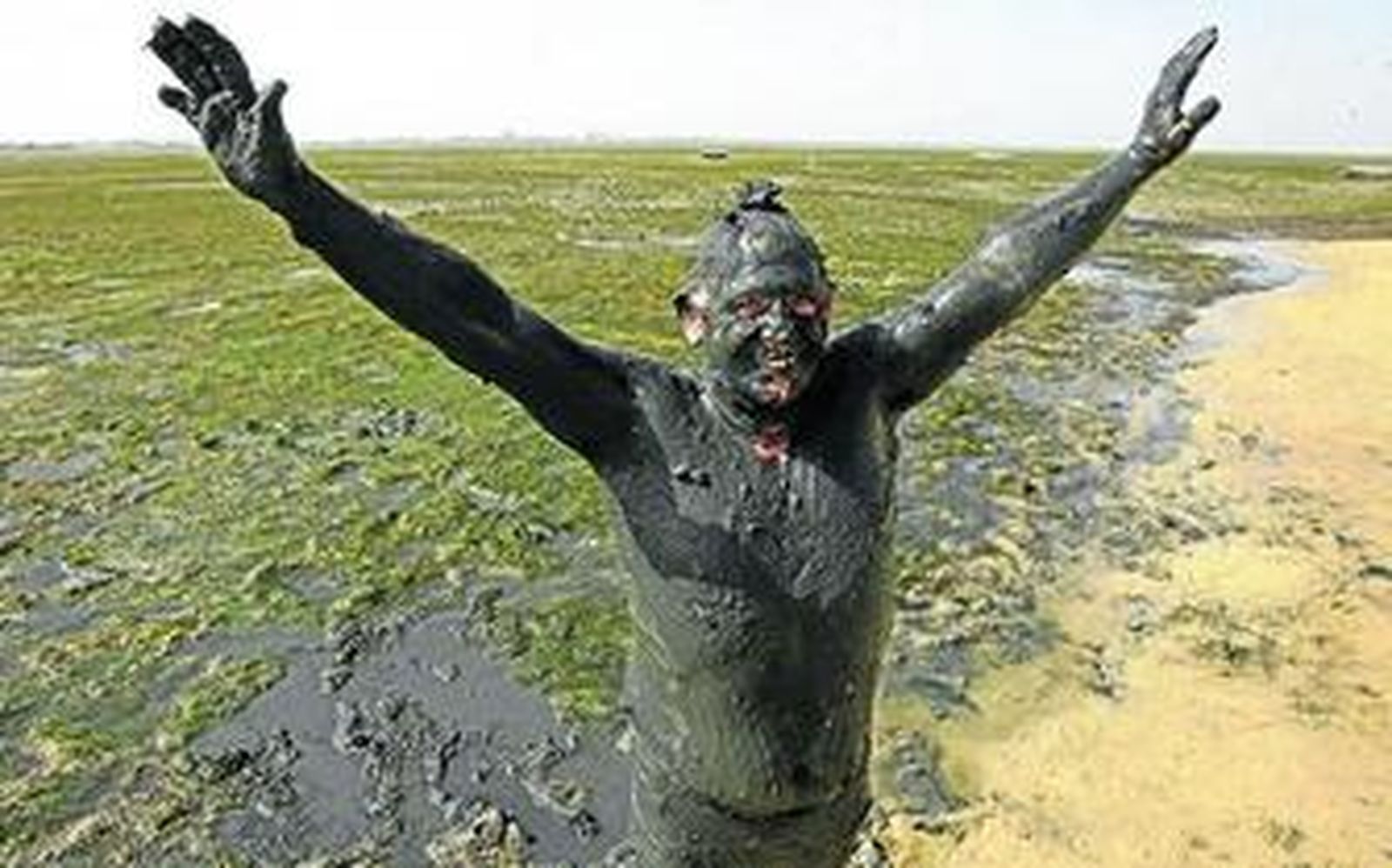 Un hombre embadurnado de fango en la playa de La Cachucha