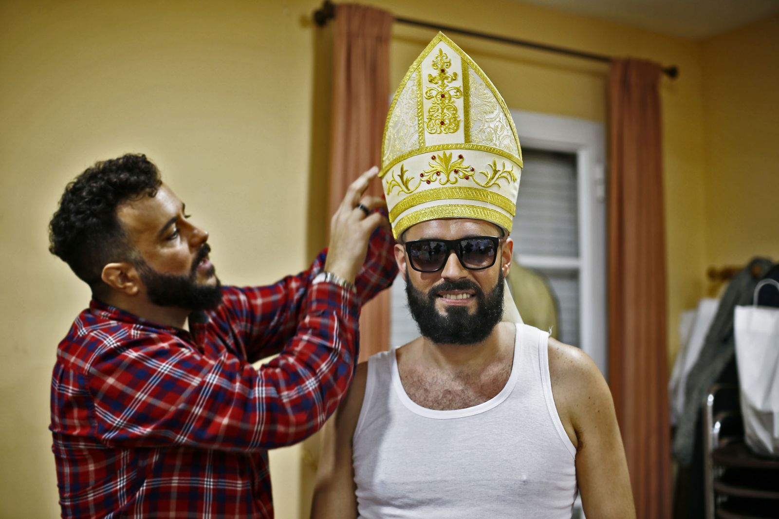 Uno de los componentes de la comparsa se coloca la mitra y las gafas de sol antes de enfundarse en la ropa de obispo.