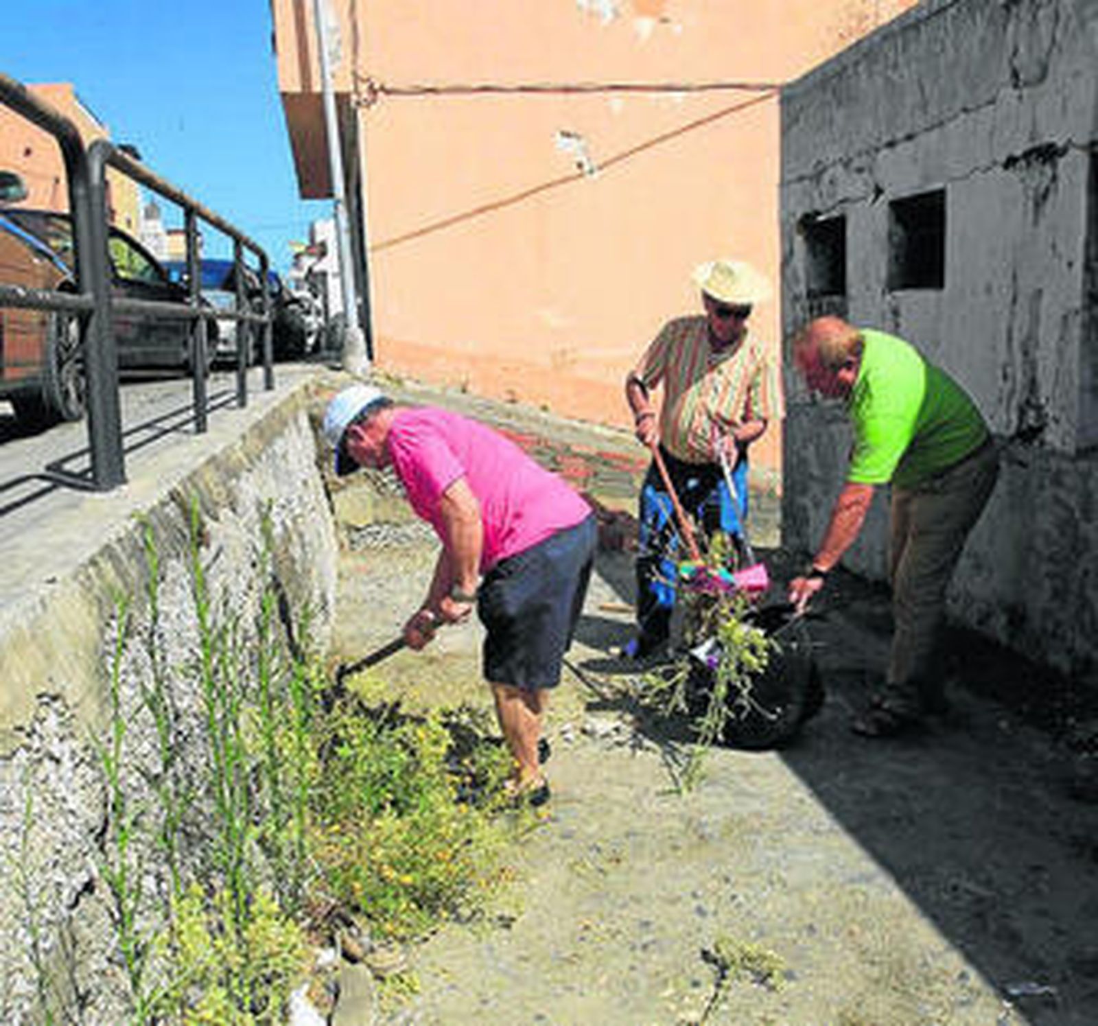 Tres vecinos limpian unas de las calles junto a la Carretera del Cobre.