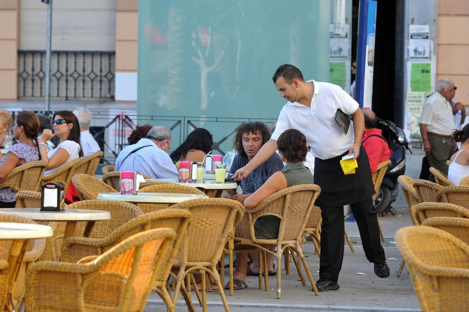 Un camarero atiende a clientes en una terraza.