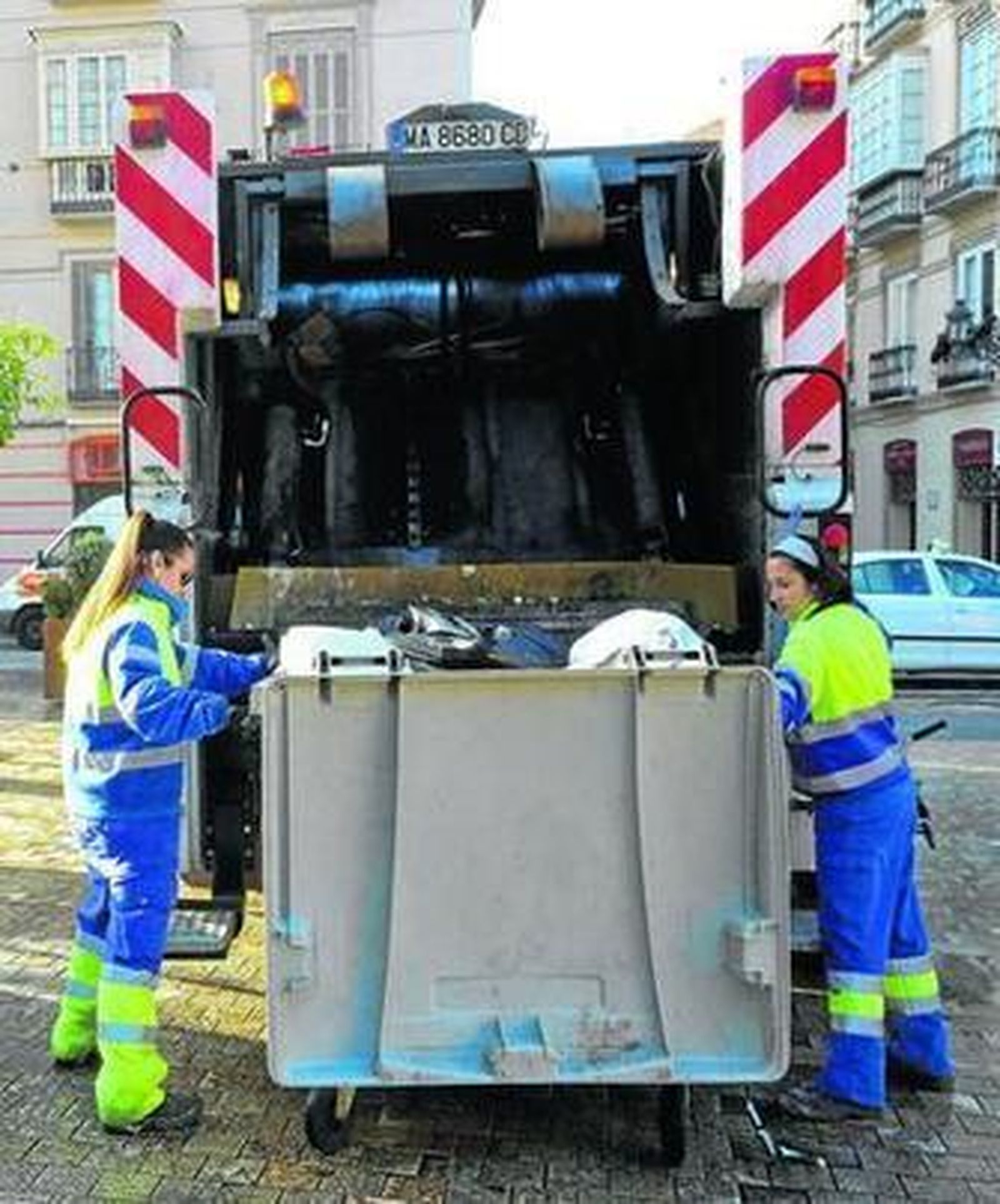 Dos trabajadoras de Limasa vacían un contenedor de basura en un camión.