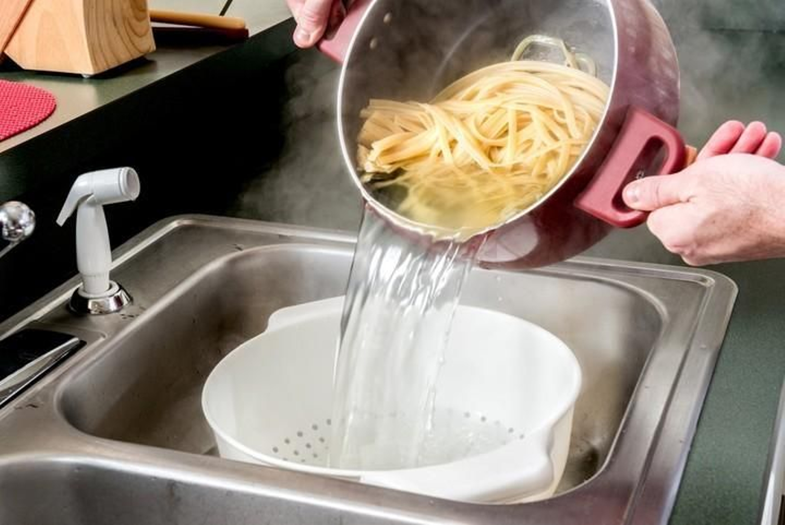 Una persona tirando el agua de la pasta en el fregadero