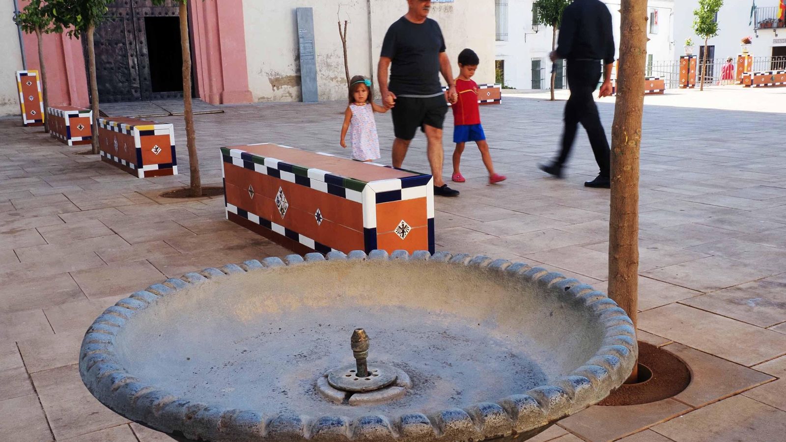 Una familia pasa junto a una fuente de beber seca en la plaza de Higuera de la Sierra