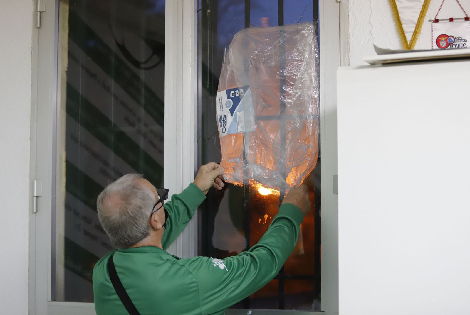 El presidente de la asociación vecinal cubre con un plástico la rotura en una ventana.