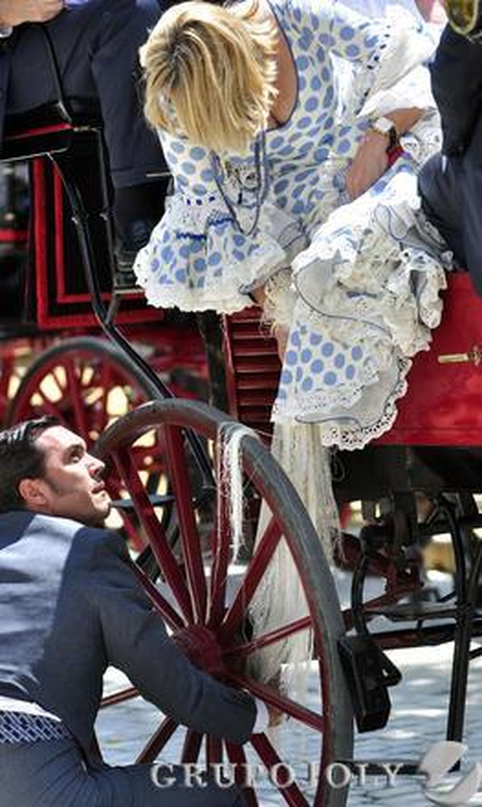 Una joven enreda los flecos de su mantón en la rueda de un coche de caballo.

Foto: Manuel Gómez