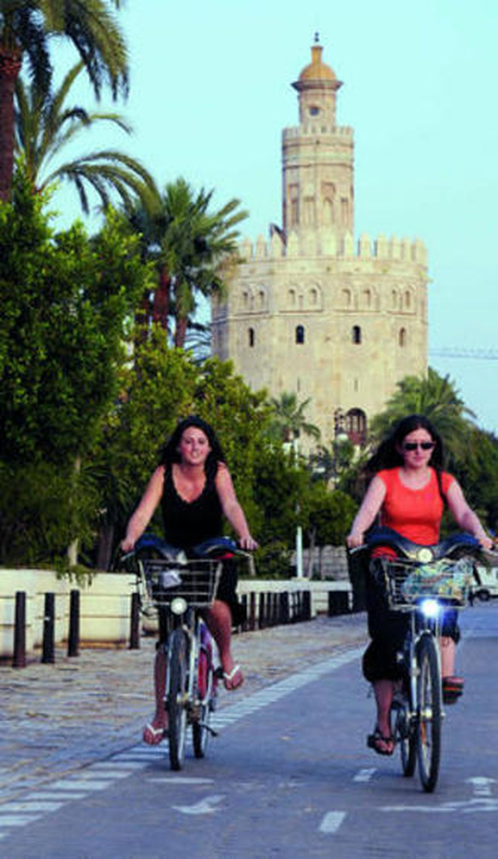 Dos jóvenes circulan en bicicletas públicas junto al río.