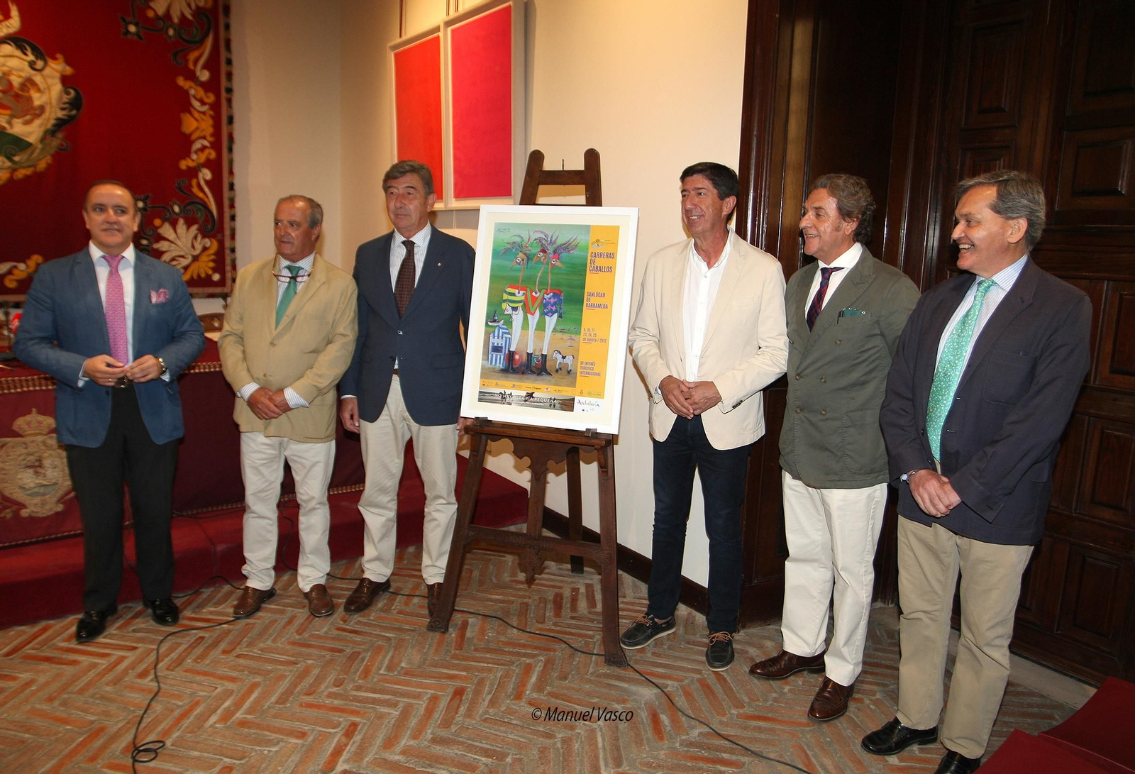 El autor del cartel, junto a su obra y el resto de personalidades que acudieron a la presentación.