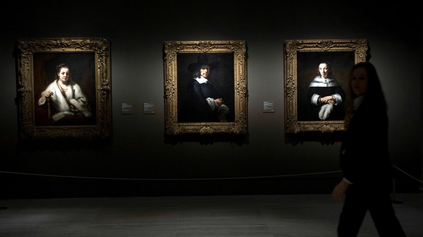Una mujer camina frente a tres retratos de Rembrandt.