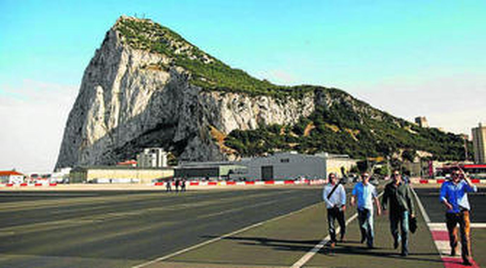 Varias personas transitan por el campo de aviación, con el Peñón al fondo.