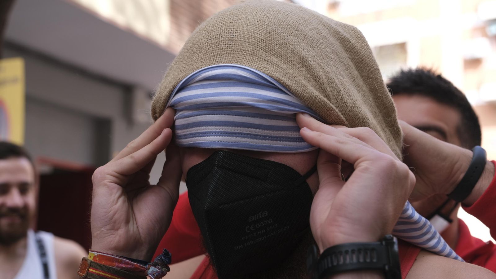 Un costalero del Resucitado se ajusta el costal, con su mascarilla bien colocada.