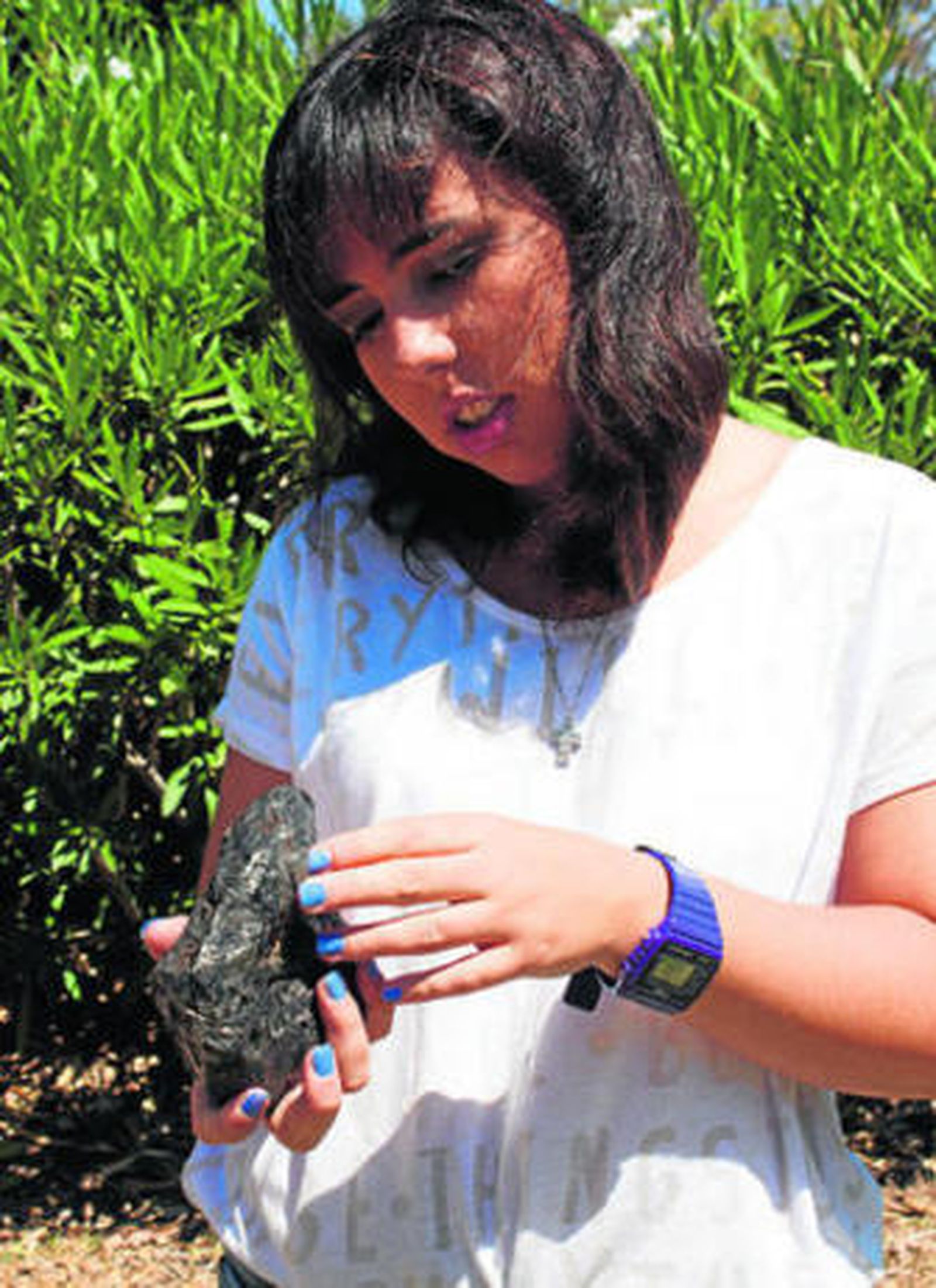 Arriba, una joven coge entre sus manos el meteorito recién adquirido por el Observatorio Astronómico. Abajo, una comparativa entre el objeto rocoso y una moneda de 1 euro.