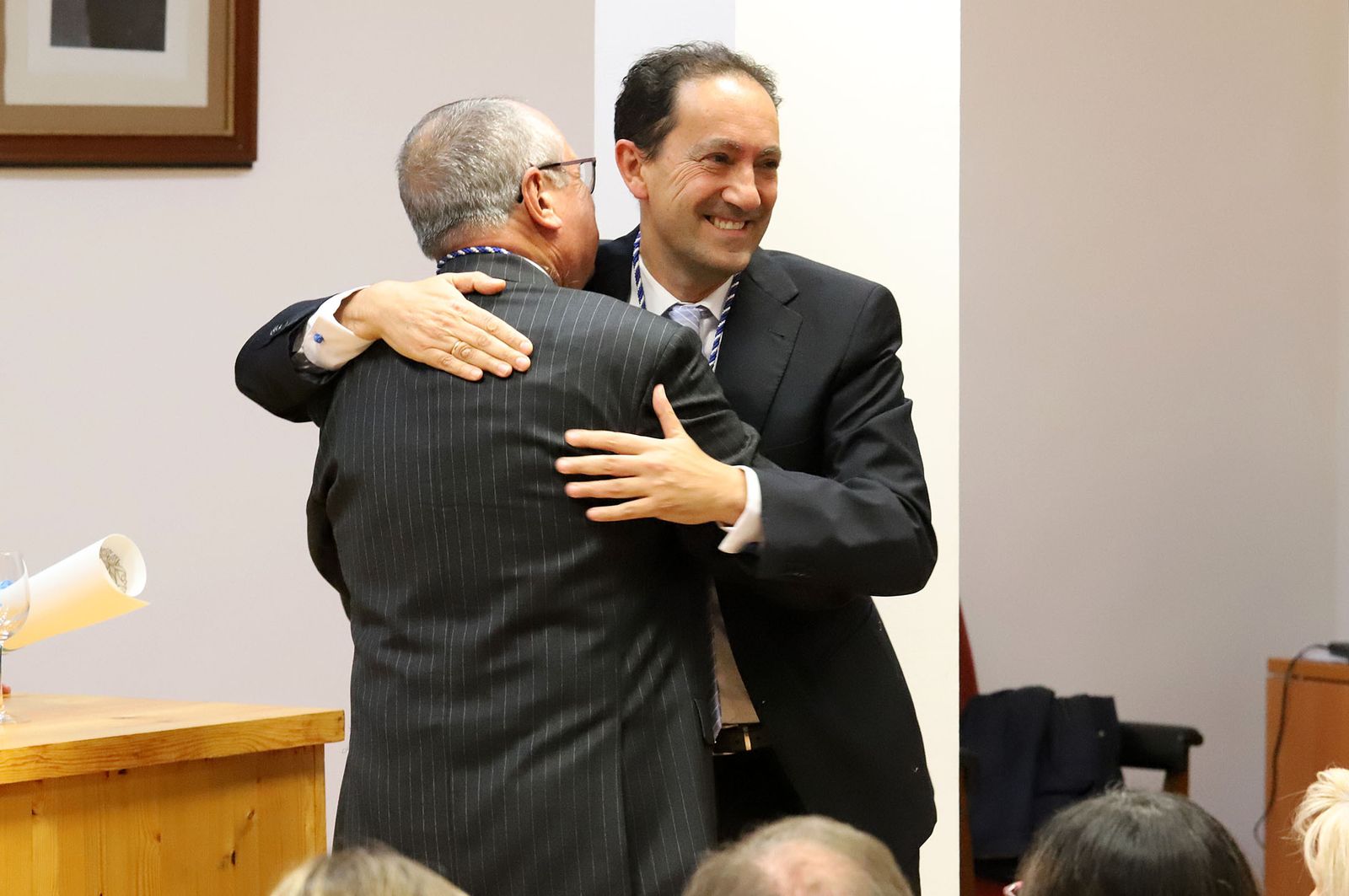 El presidente de la Academia, Emilio Pascual (de espaldas), abraza a Juan Bayo tras imponerle la medalla.
