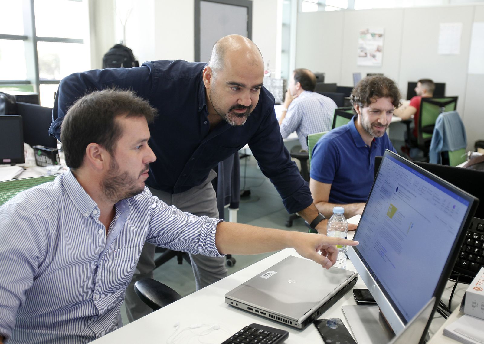 Juan Carlos Rubio, de pie, atiende a las explicaciones de un miembro del equipo de QosIT en la sede central de la consultoría, en Camas (Sevilla).