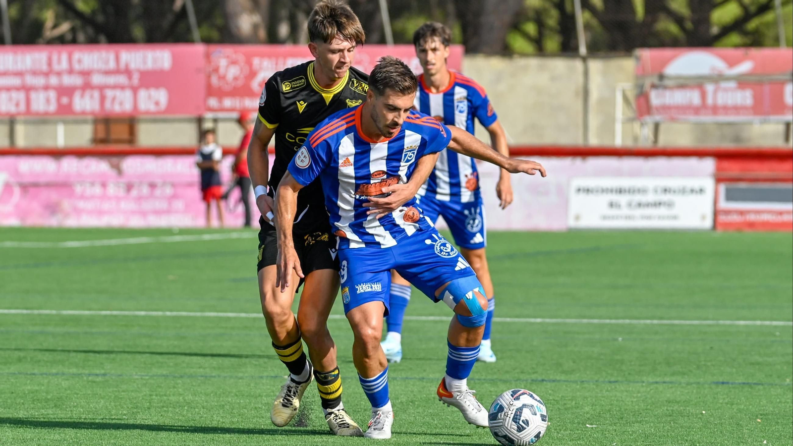 Zelu controla el balón mientras es agarrado por Kikín, con Leo Vázquez al fondo.