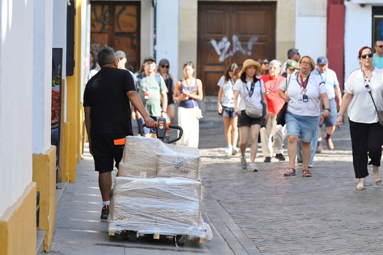 Un trabajador traslada una carretilla por el Casco Histórico junto a un grupo de turistas.