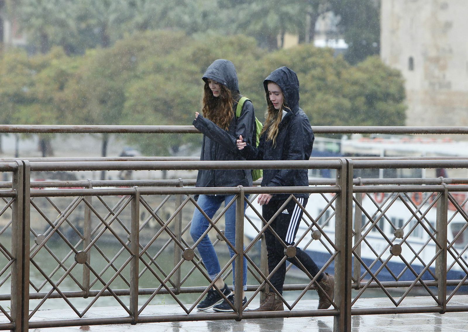 Dos chicas caminan bajo la lluvia por el puente de San Telmo.