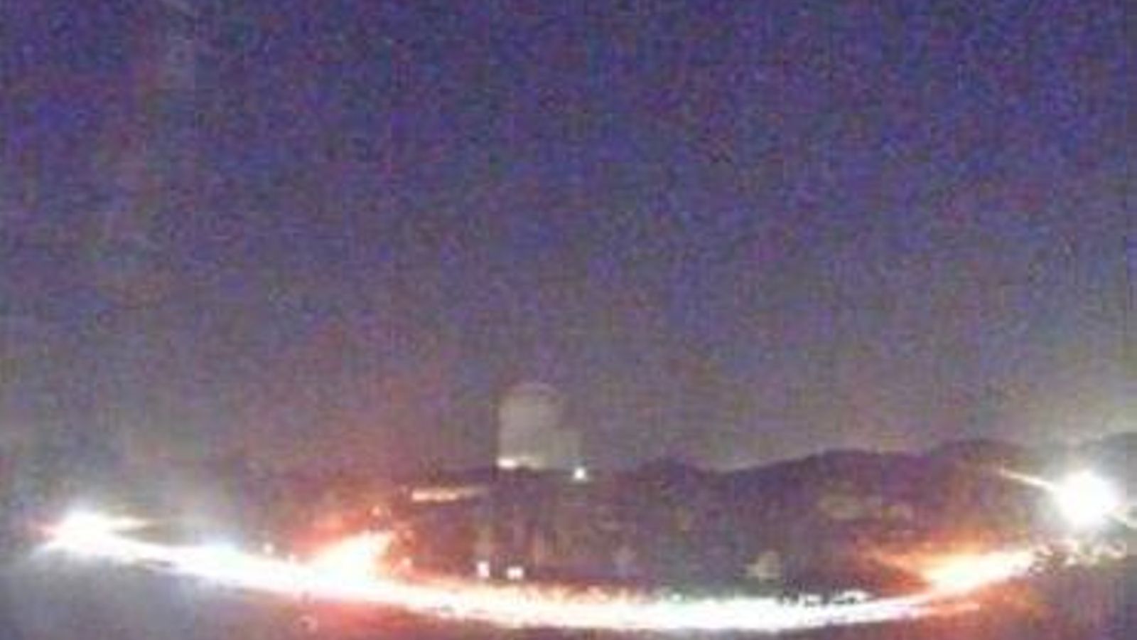 una imagen tomada una noche de agosto del año 2021, que muestra el impacto de las luces de una larga fila de coches que llegan a hacer visible la cúpula de uno de los telescopios.