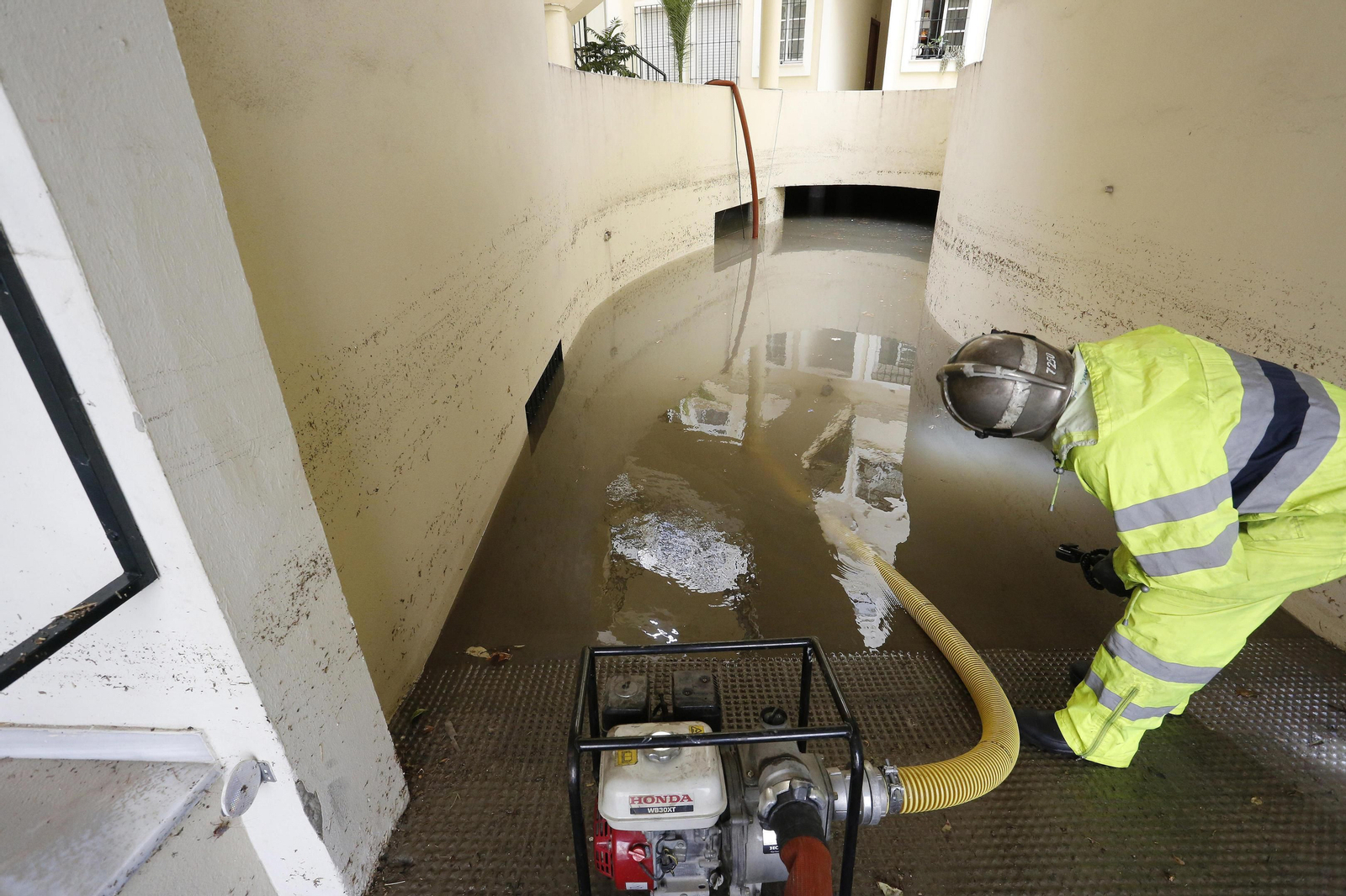 Un bombero achica agua de un garaje de calle Arcos completamente anegado con varios vehículos en su interior.