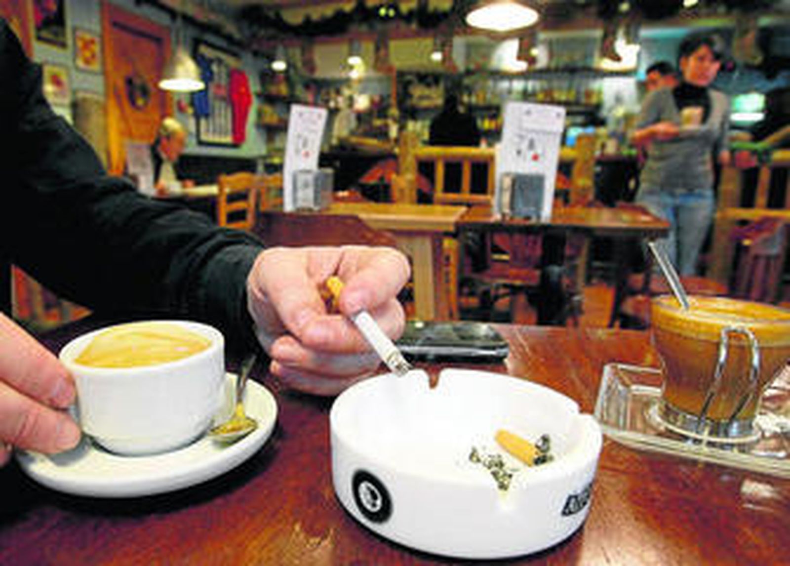 Un hombre se fuma un cigarrillo en una cafetería mientras se toma un café.