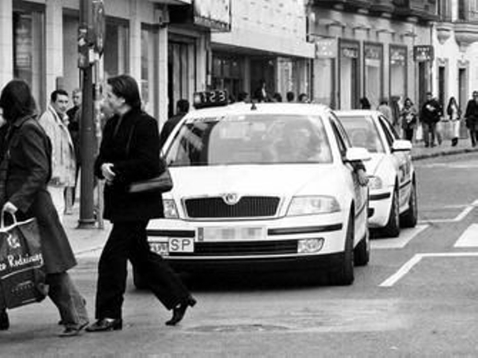 Dos peatones cruzan por la Plaza del Duque de Sevilla, a pocos metros de un taxi con emisora.