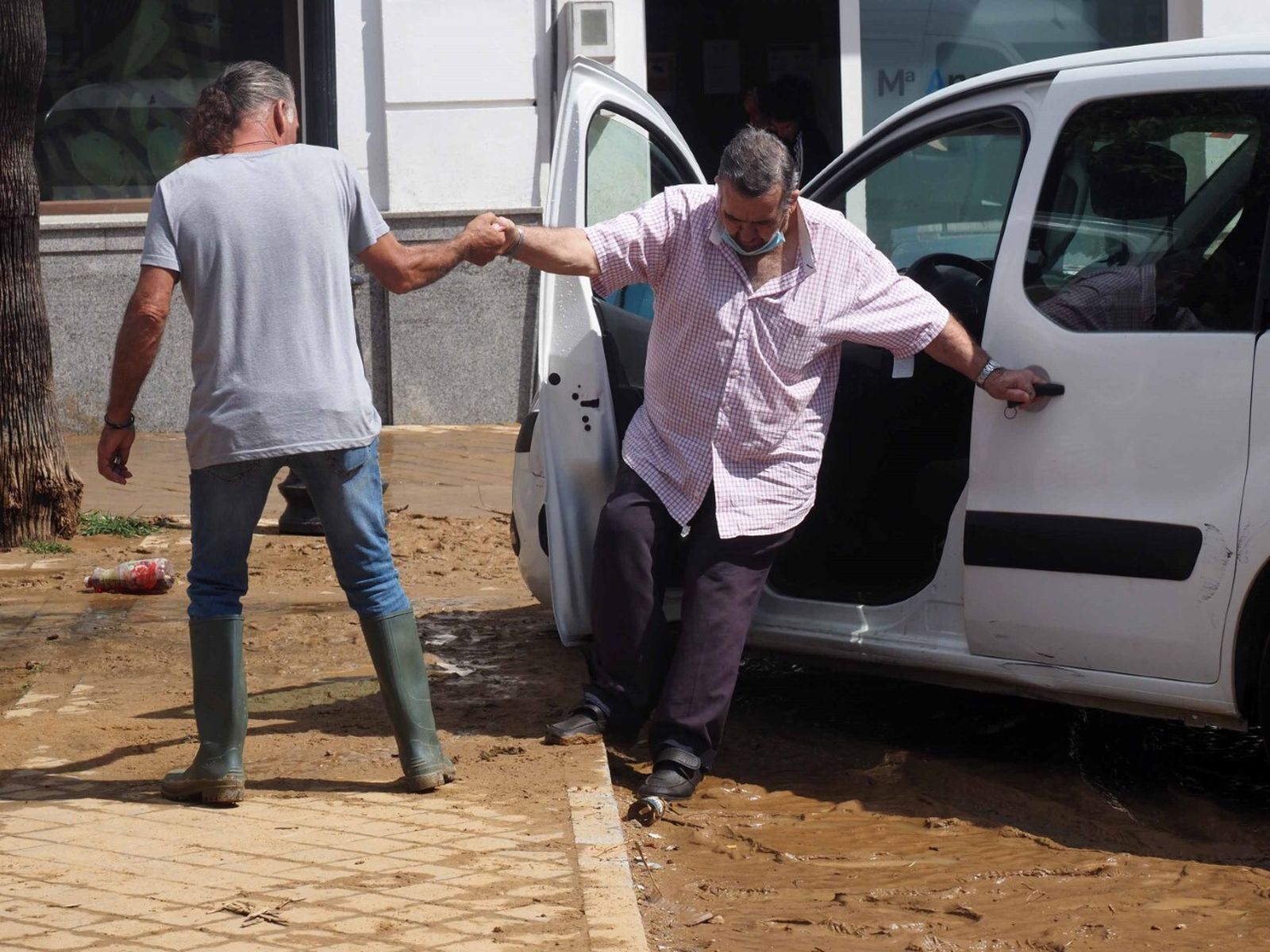 Un vecino ayuda a otro a salir de su vehículo en una calle llena de fango.