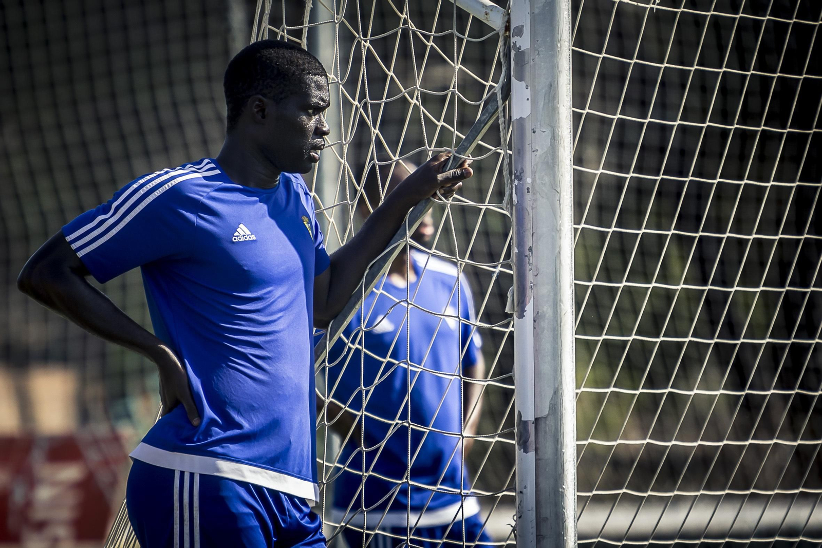 Sankaré fija la mirada en el trabajo de sus compañeros mientras se agarra a la red de una portería del campo 4 de El Rosal.