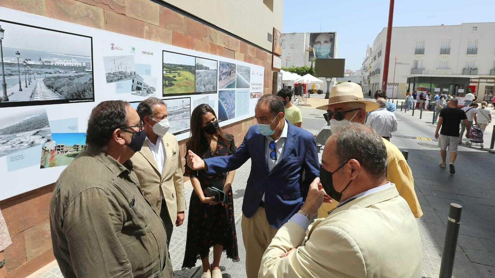 Los asistentes al acto de inauguración de la exposición conversan ante los paneles de la muestra.