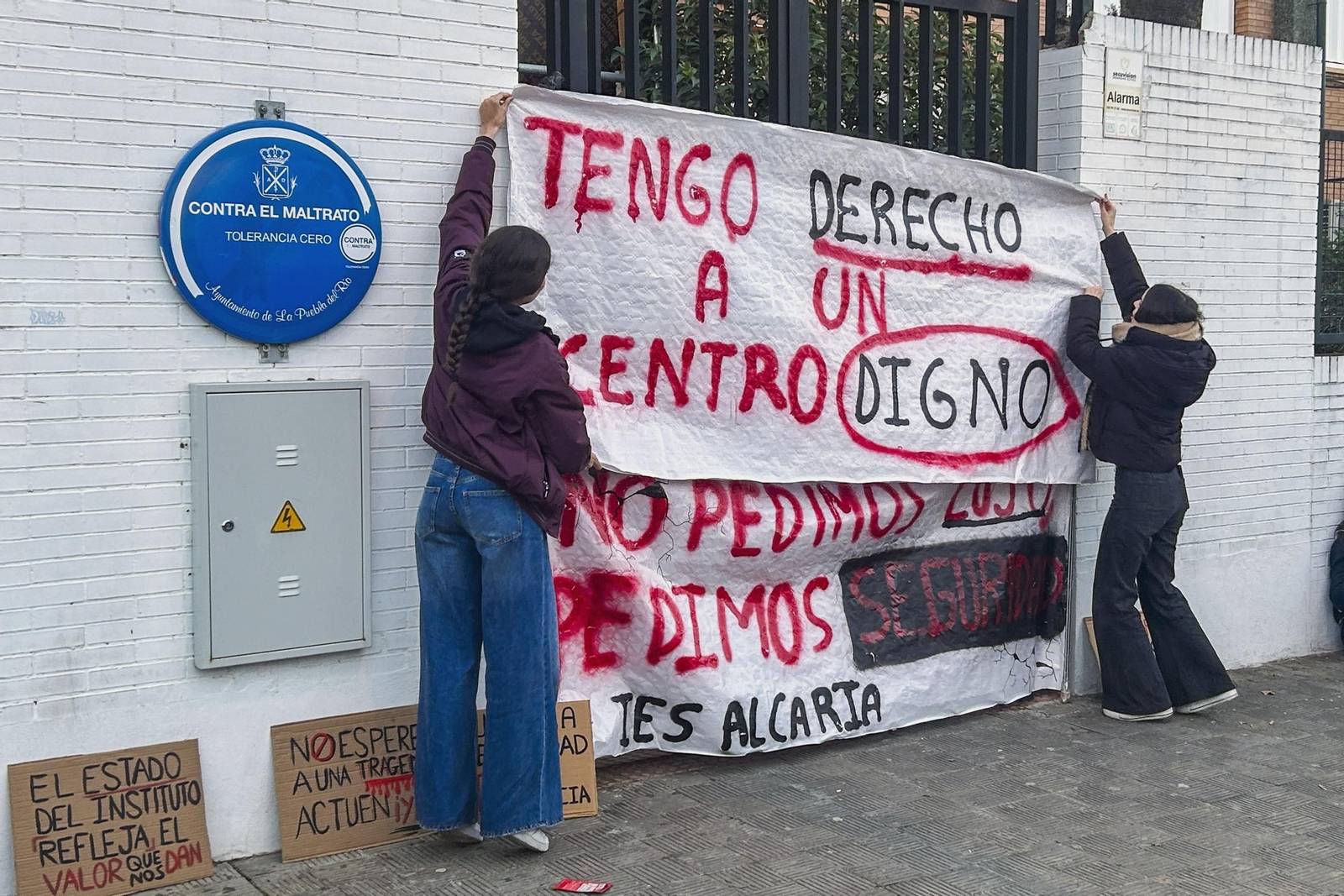 Dos alumnas colocan pancartas en la fachada del IES Alcaria, en la Puebla del Río.