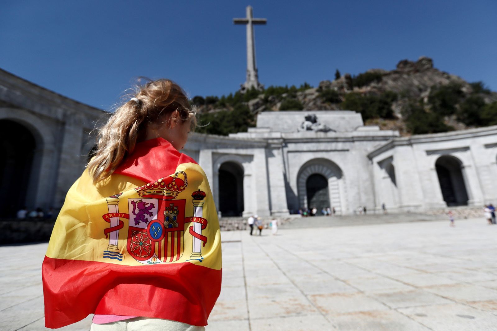 Una mujer envuelta en una bandera nacional ante la entrada de la basílica del Valle de los Caídos.