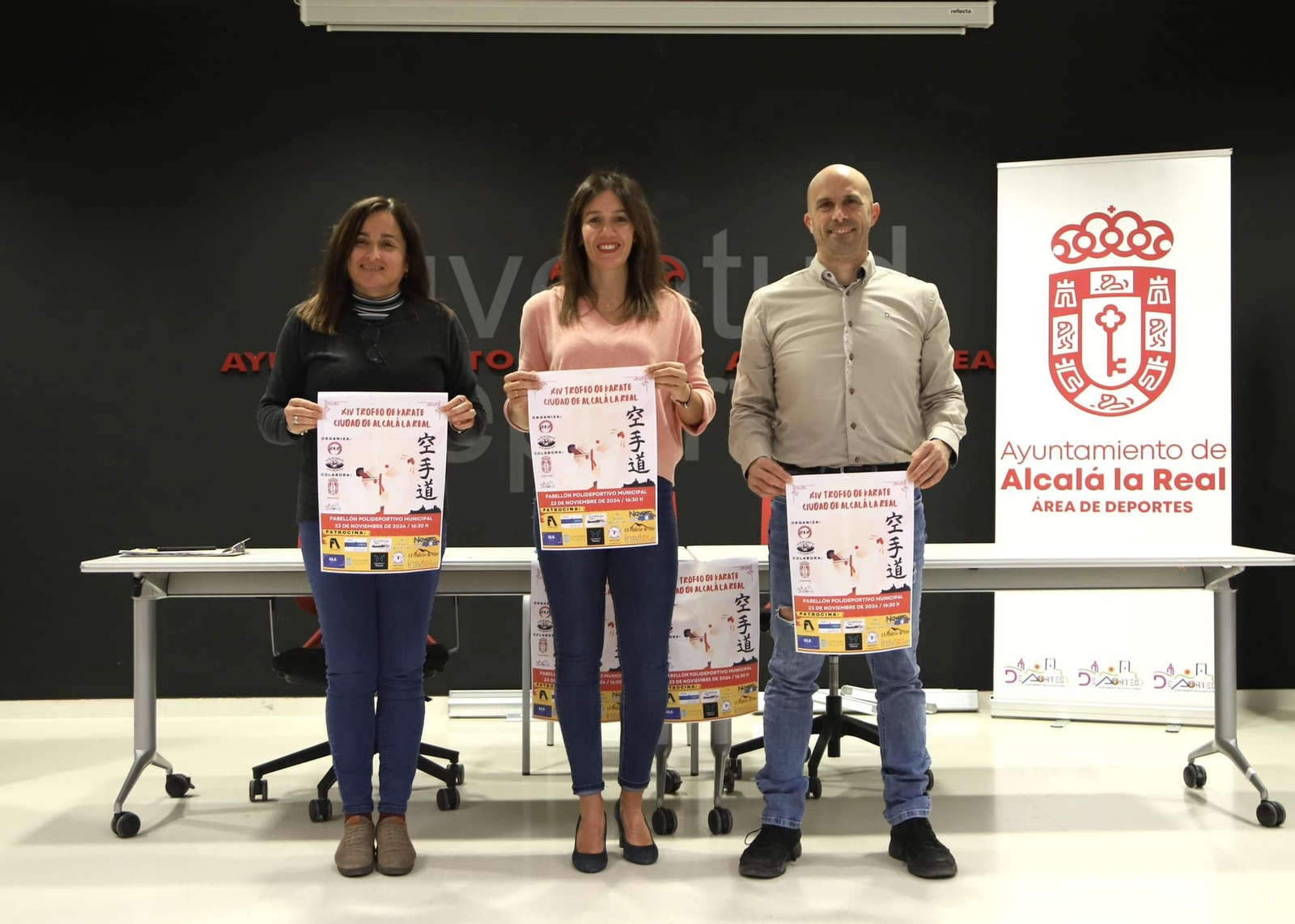Eva Hinojosa, Belén Ramírez y Álvaro Rosales posan con el cartel del evento.