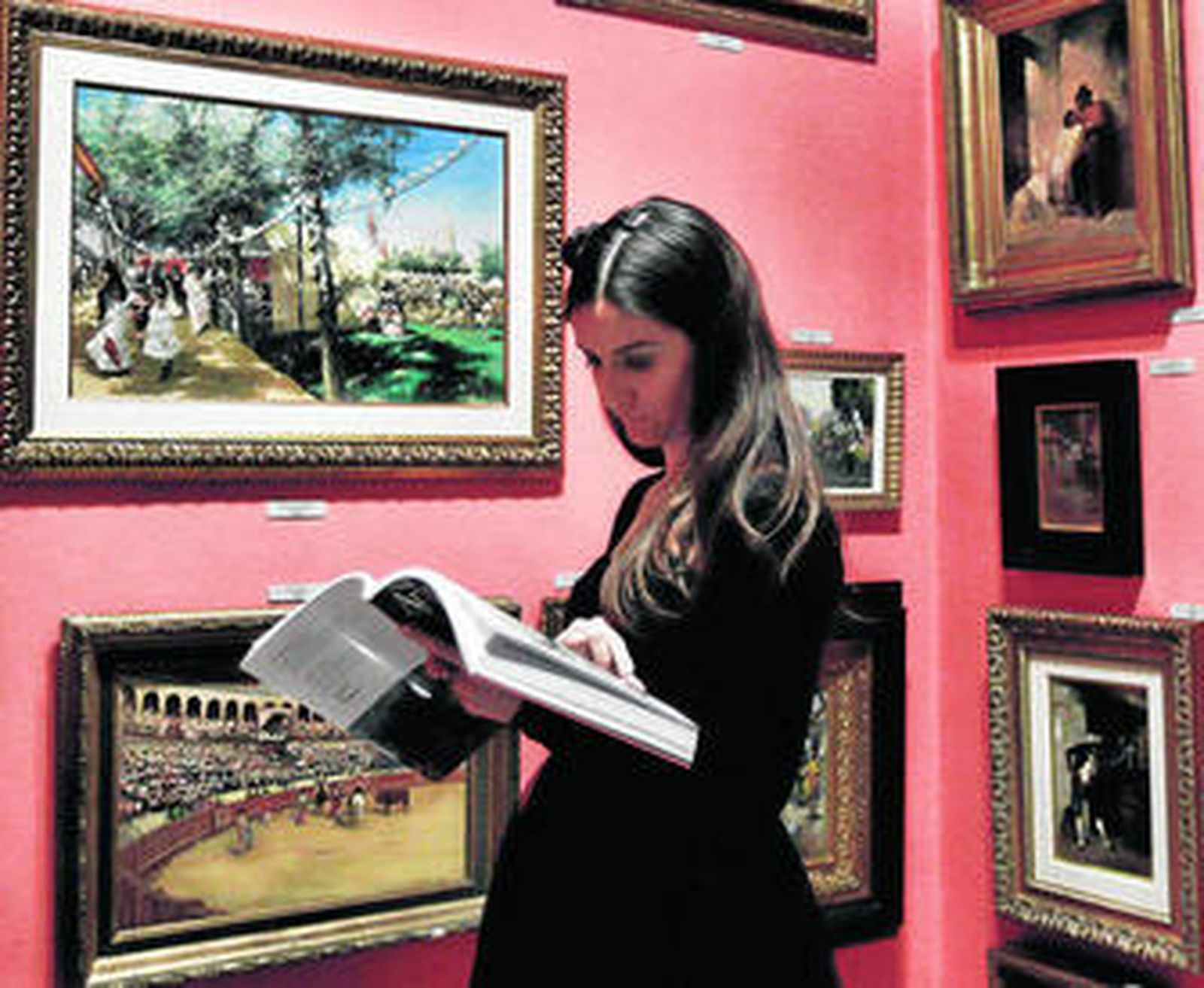 Una visitante a la exposición de la subasta consulta el catálogo frente al cuadro 'Feria de Sevilla'.