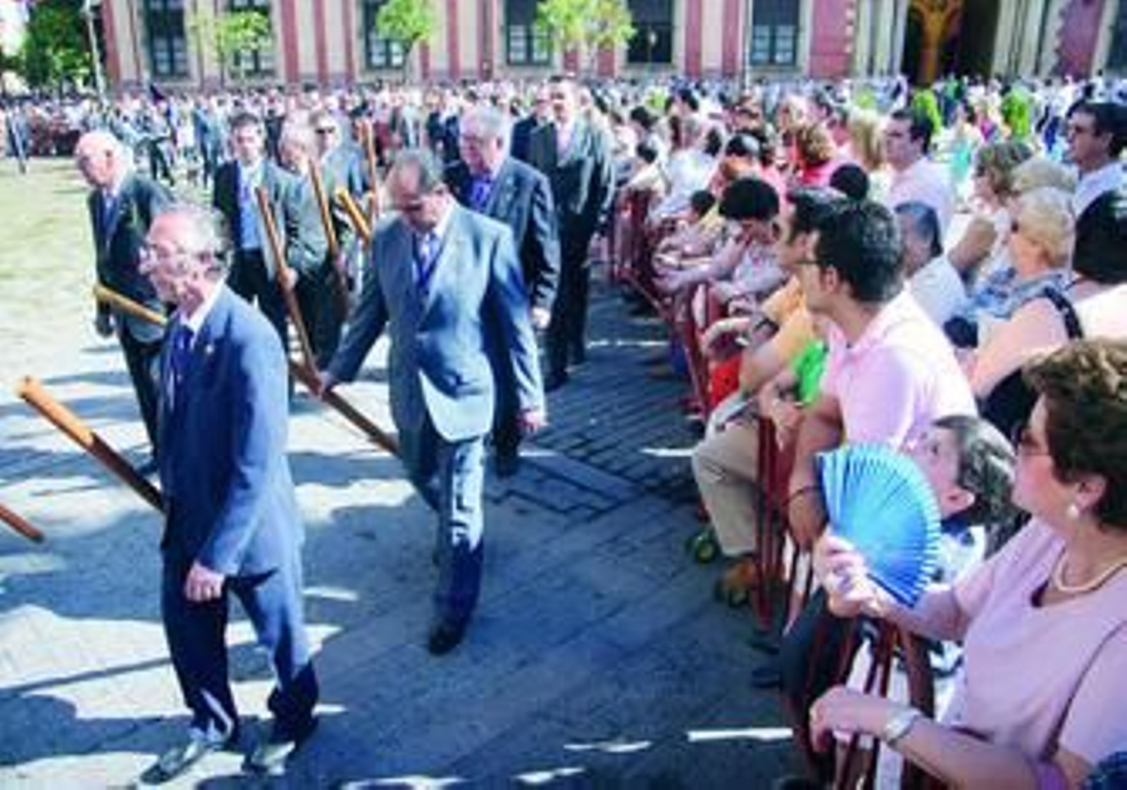 Asistentes a la fiesta del Corpus contemplan el cortejo en la plaza Virgen de los Reyes.